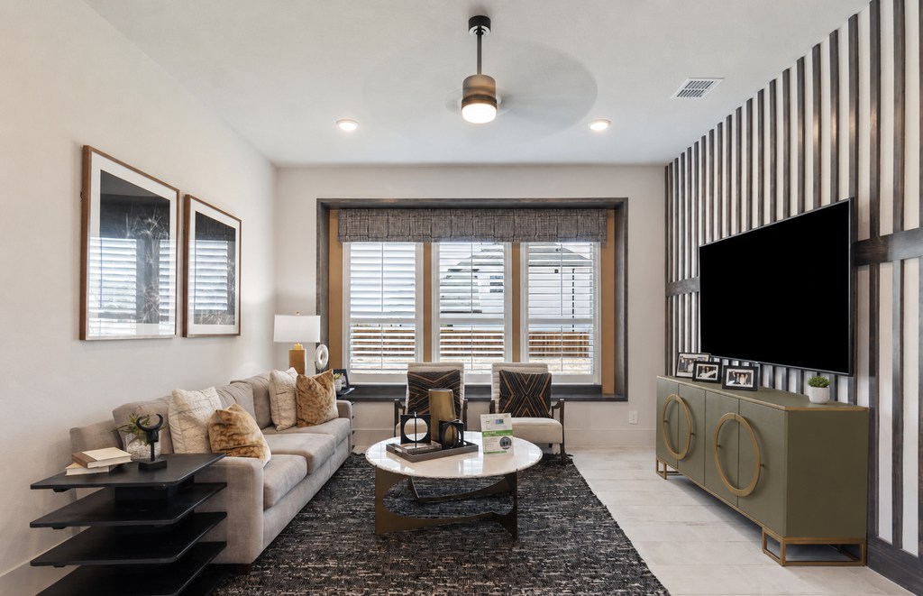 Modern living room with a muted olive green TV console, brass ring handles, slatted accent wall, neutral sofa, black rug, and warm metallic decor.