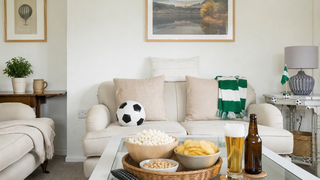 Bright living room prepared for World Cup viewing with popcorn, chips, drinks, a remote, soccer ball, green scarf, and festive accents.