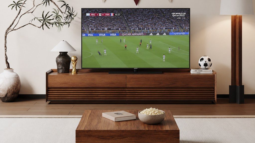 Modern living room with a wood TV console, a World Cup soccer match playing on the television, subtle soccer decor, and popcorn on the coffee table.
