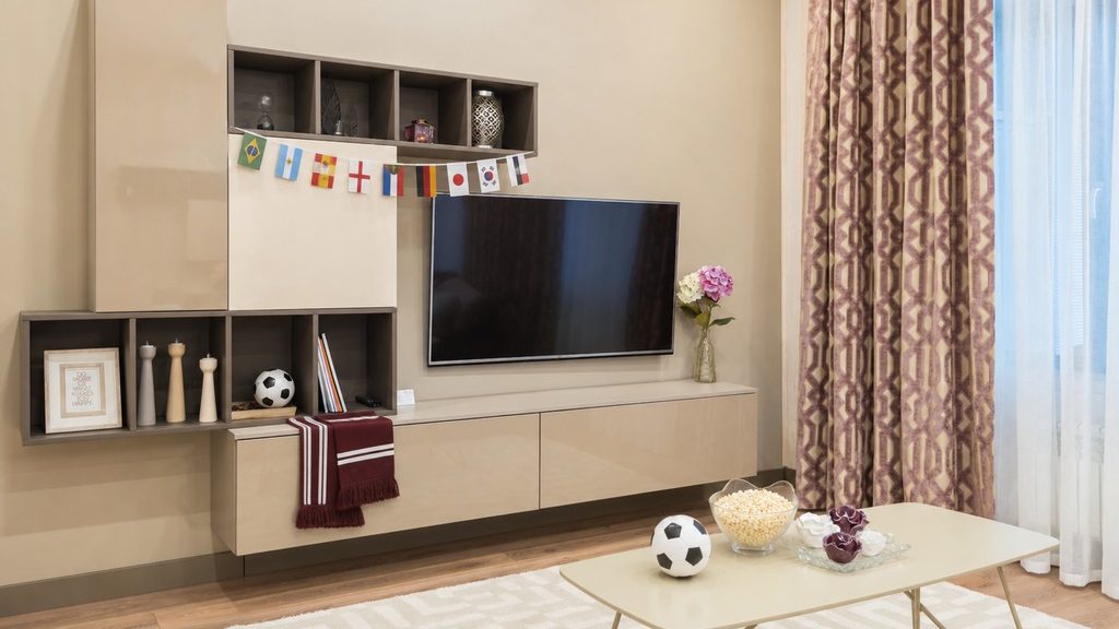Modern living room with a built-in media wall, international soccer flags, a fan scarf, soccer balls, and popcorn set out for a World Cup watch party.