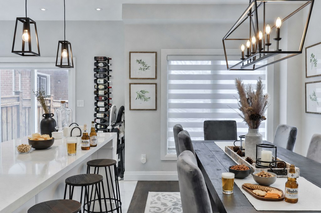 Modern open-plan kitchen and dining room with beer, chips, nuts, crackers, and cheese arranged on the island and dining table for casual game-day hosting.