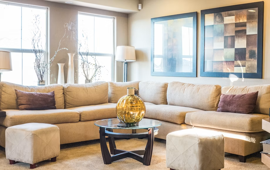 Warm beige modern sofa sets featuring a large sectional couch, twin footstool ottomans, and a glass coffee table.