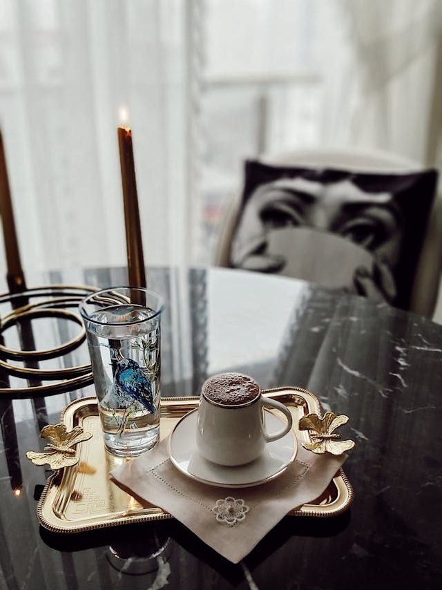 a tray with a cup of water and a cup of coffee on a black marble coffee table near two candles in a bright and luxurious living room