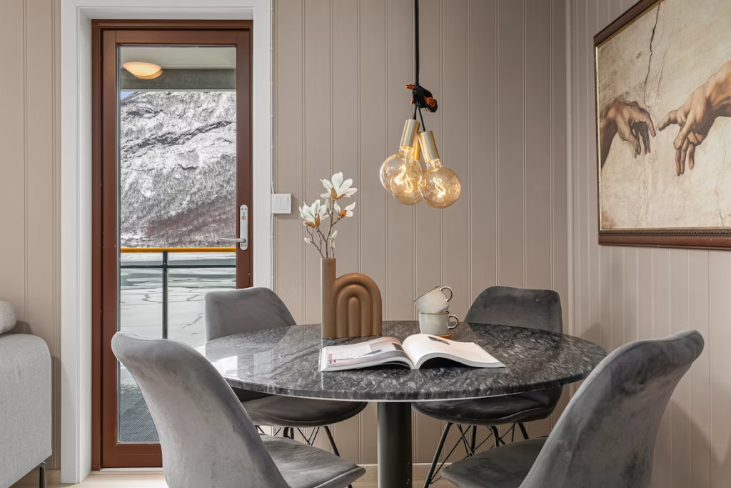 Compact dark grey round sintered stone table with plush velvet chairs under warm pendant lighting in a cozy dining area.