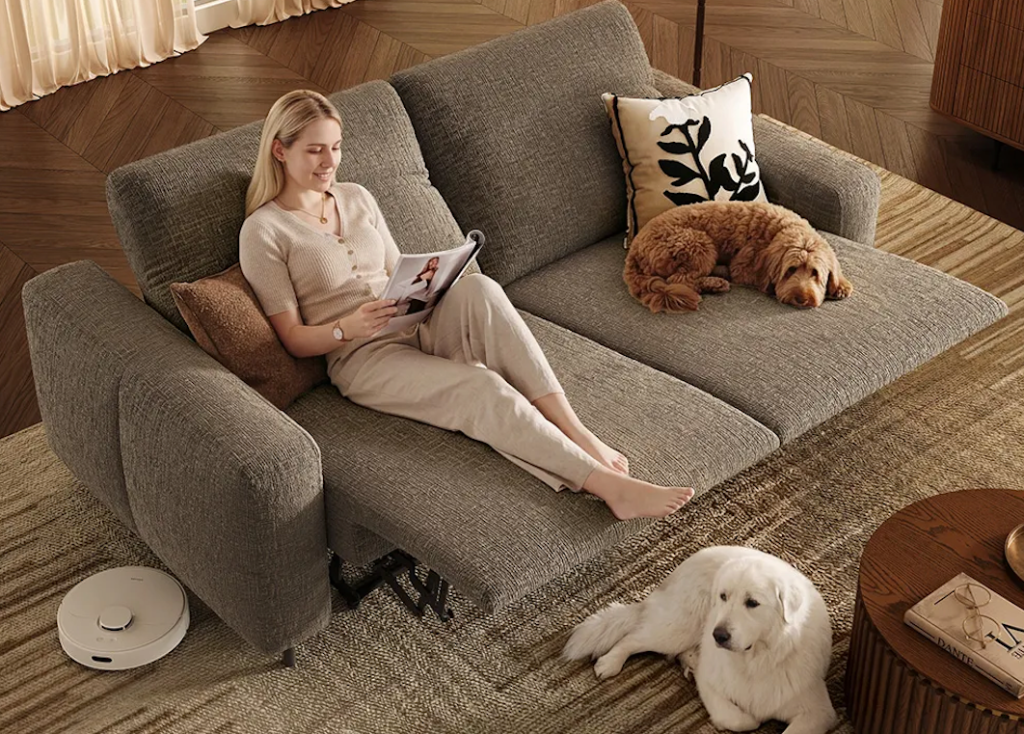 Top view of a grey fabric power reclining loveseat with a woman reading, flanked by two dogs.