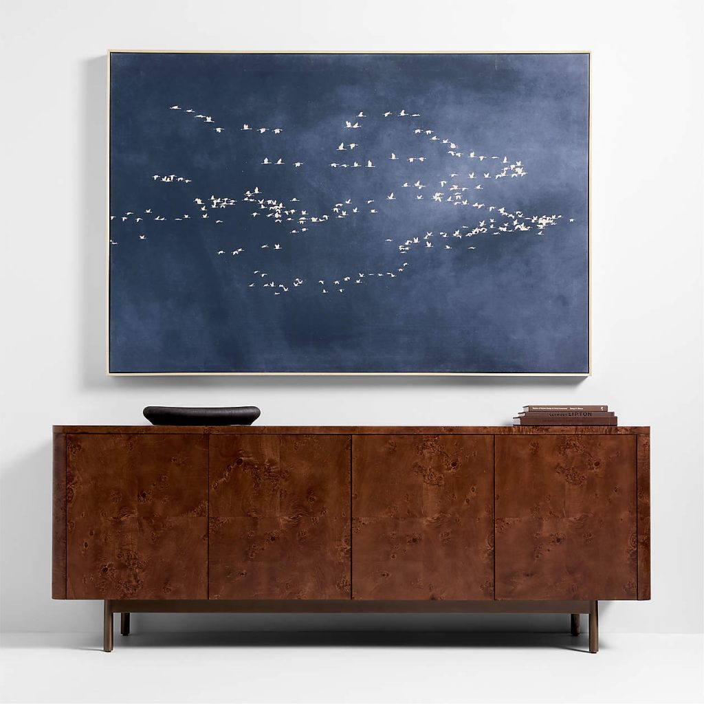 Crate & Barrel Mota 80" Burl Wood Storage Media Console with books and a tray on top below a wall-mounted painting in a minimalist room