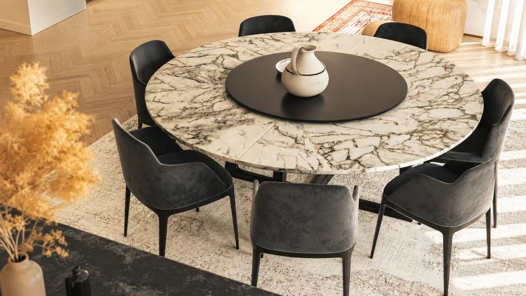 Large round sintered stone table featuring luxury marble veining, a black lazy Susan turntable, and dark grey velvet chairs.