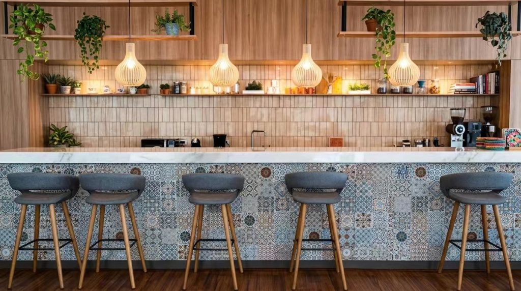 Comfortable mid-century bar stools with grey upholstered seats arranged along a vibrant, patterned tile bar wall.