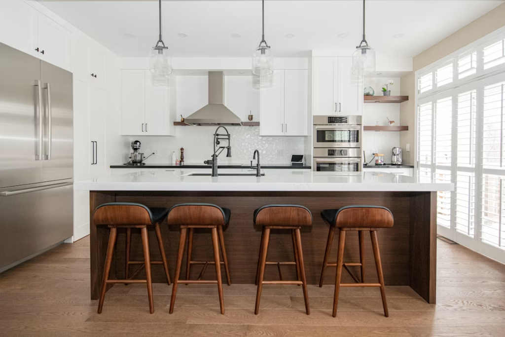 Four mid-century modern wooden bar stools with dark leather seats positioned at a sleek, white-topped kitchen counter.