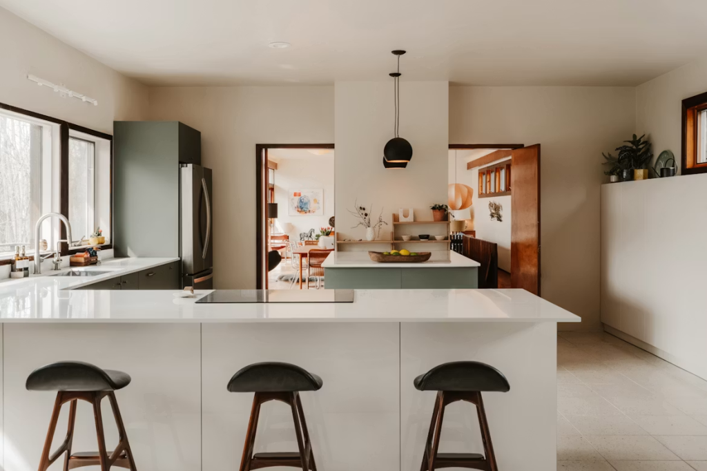 High-end mid-century bar stools with dark wood frames and black leather seats under a clean white kitchen island.