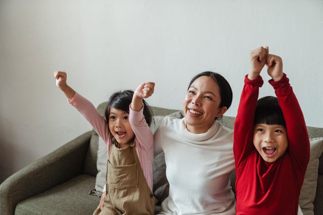 Mother and children cheering joyfully on a sofa, celebrating together