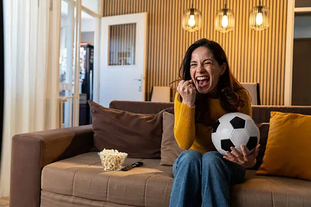 a woman celebrating a soccer goal on sofa