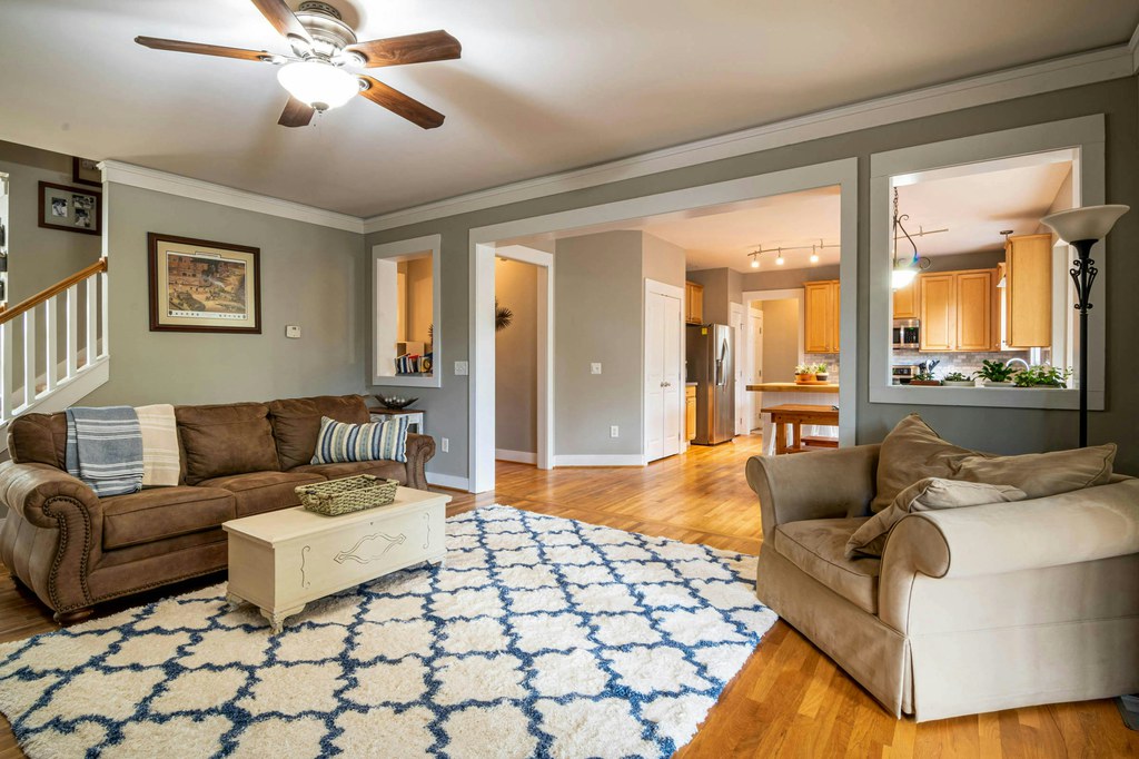 Cozy family room with a brown sofa, upholstered armchair, patterned area rug, and coffee table in an open layout beside the kitchen.