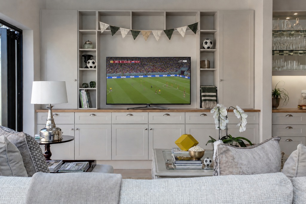 Modern living room with built-in TV storage, subtle soccer decor, popcorn on the coffee table, and a World Cup match playing on the television.