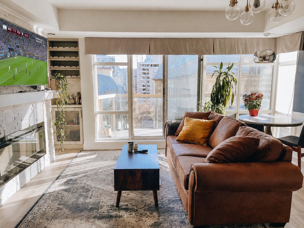 Bright apartment living room with a brown leather sofa, coffee table, fireplace TV wall, and a live World Cup soccer match playing on the television.