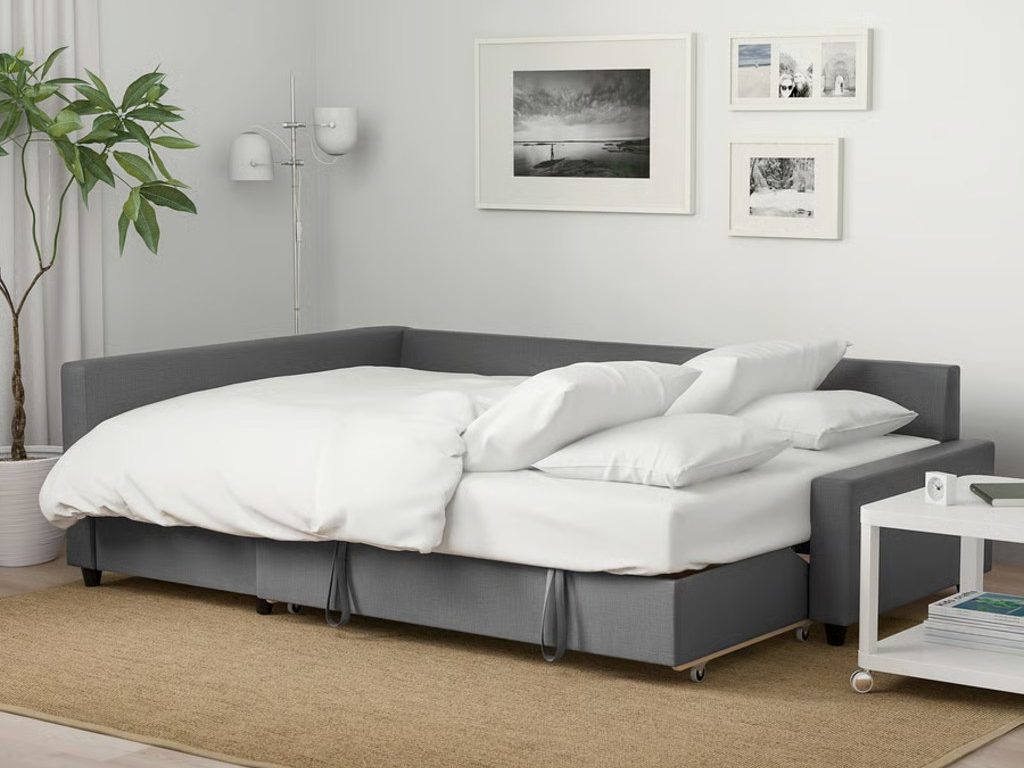 Gray sectional sleeper sofa unfolded into a bed with white bedding and pillows in a modern living room.