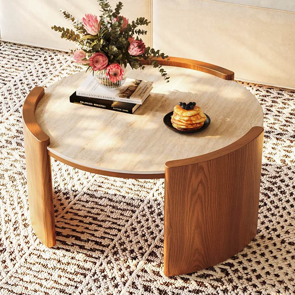 Round marble-look coffee table with warm walnut wood legs, styled with a flower vase, stacked books, and pancakes on a patterned rug.