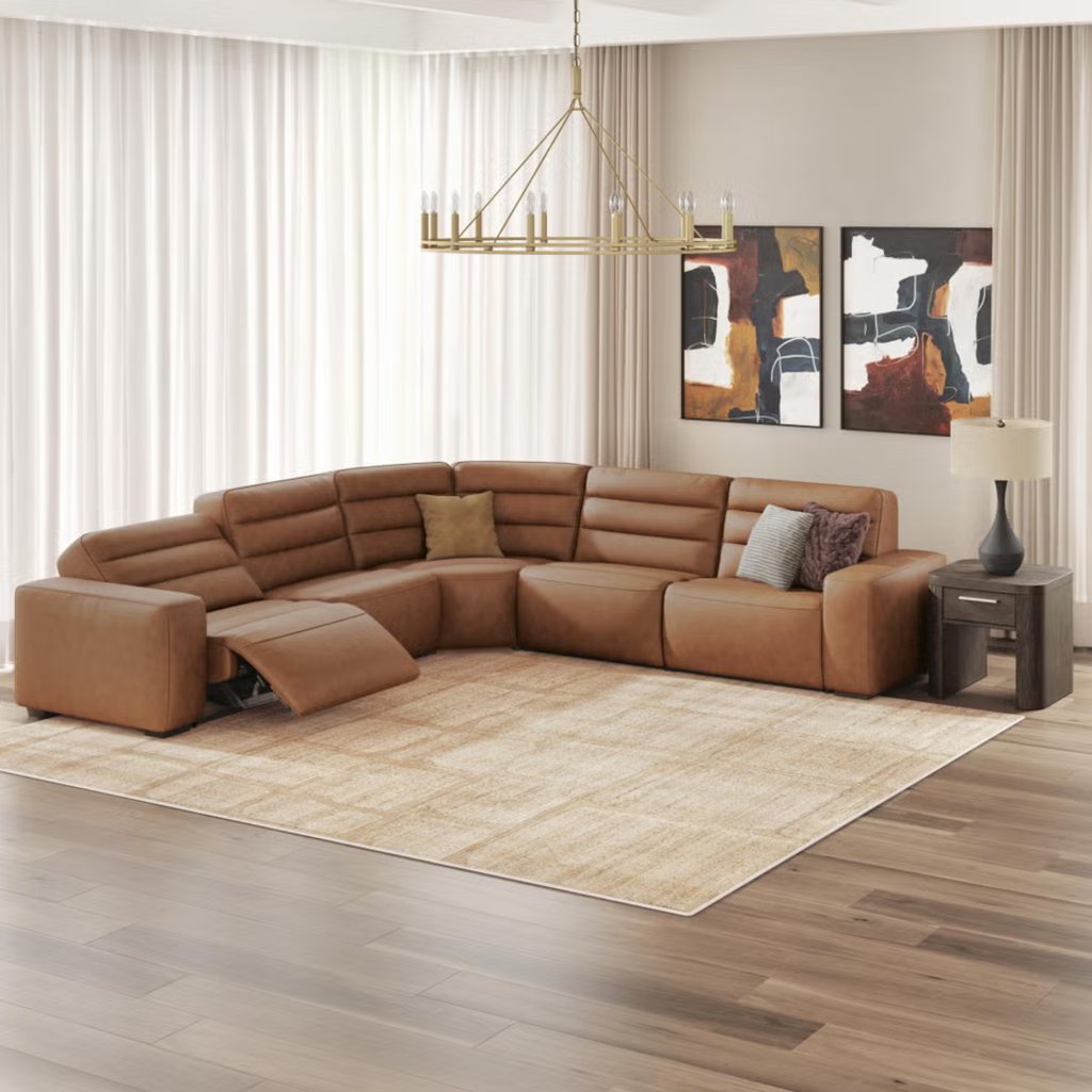 Brown leather reclining sectional sofa with one extended footrest in a spacious modern family room with sheer curtains, abstract wall art, a large area rug, and a side table.