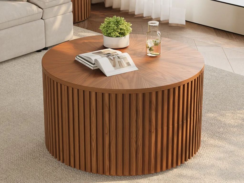 Round walnut wood coffee table with fluted sides, styled with a plant, glass carafe, and open book beside a cream sofa.