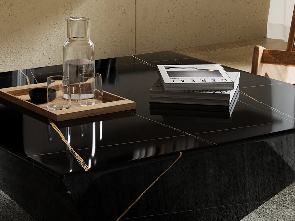 Black marble coffee table with gold veining, styled with a wooden tray, glass carafe, drinking glasses, and stacked design books.