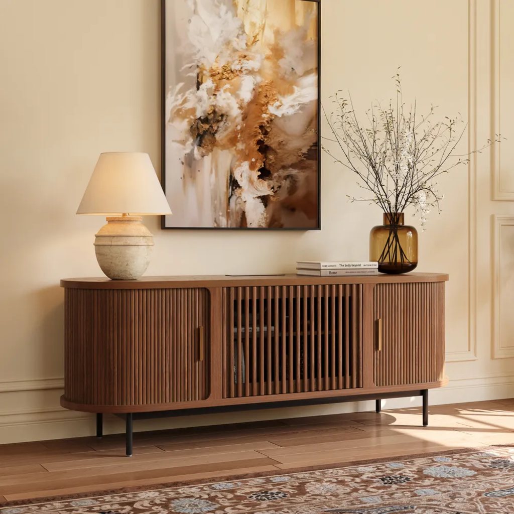 Walnut tambour door sideboard with rounded ends, brass handles, a table lamp, dried branches, and abstract artwork in a warm neutral living room.