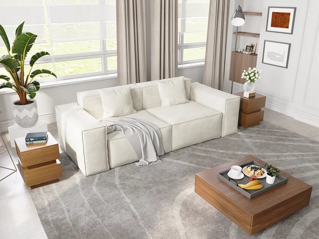 Bright living room with white modular sofa, wood coffee table, large gray rug, side tables, plants, and asymmetrical wall decor.