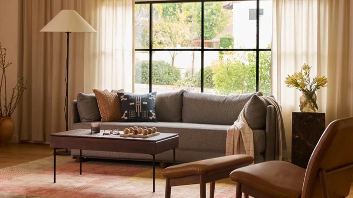 Warm living room with a gray sofa, wooden coffee table, and brown lounge chair beside a large window.