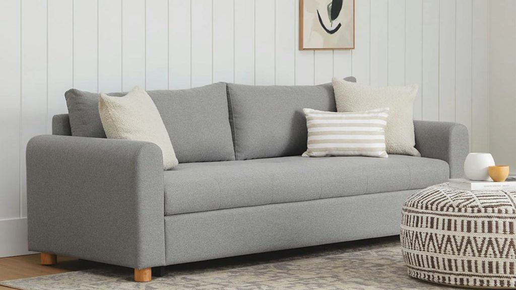 Gray sleeper sofa with neutral throw pillows in a bright modern living room.
