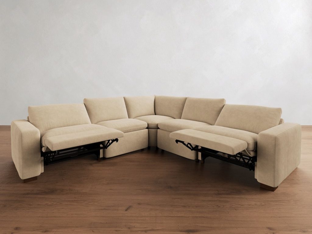 Beige reclining sectional sofa with two extended footrests and a curved corner seat, shown on a dark wood floor against a plain white wall.