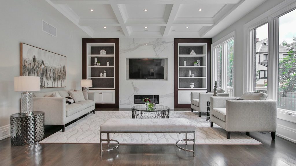 Bright living room with straight sofas, round glass coffee table, coffered ceiling, built-in shelves, large windows, and balanced horizontal and vertical lines.