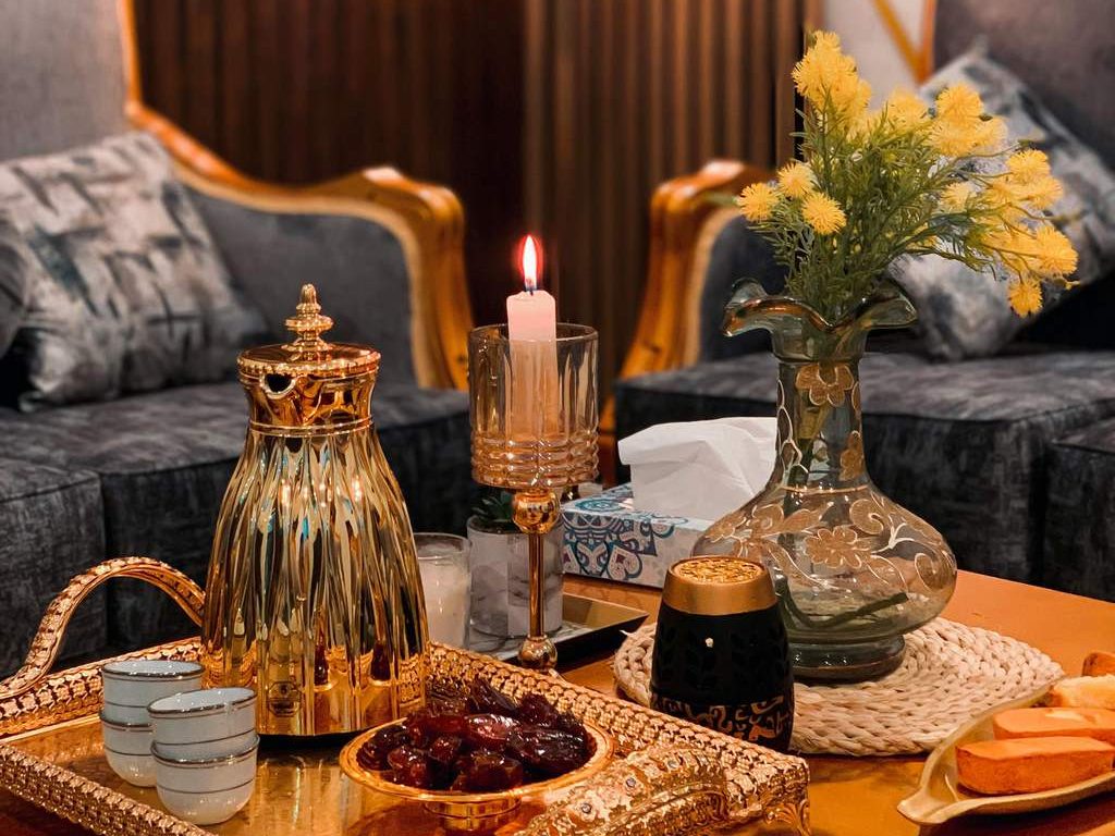 Gold decorative tray with teapot, cups, candle, flowers, and sweets on a coffee table in an elegant living room.
