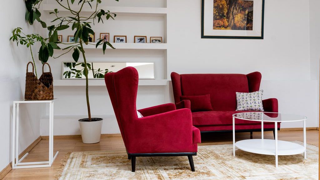 Red wingback accent chair paired with a matching loveseat, glass coffee table, and patterned rug in a bright modern living room.