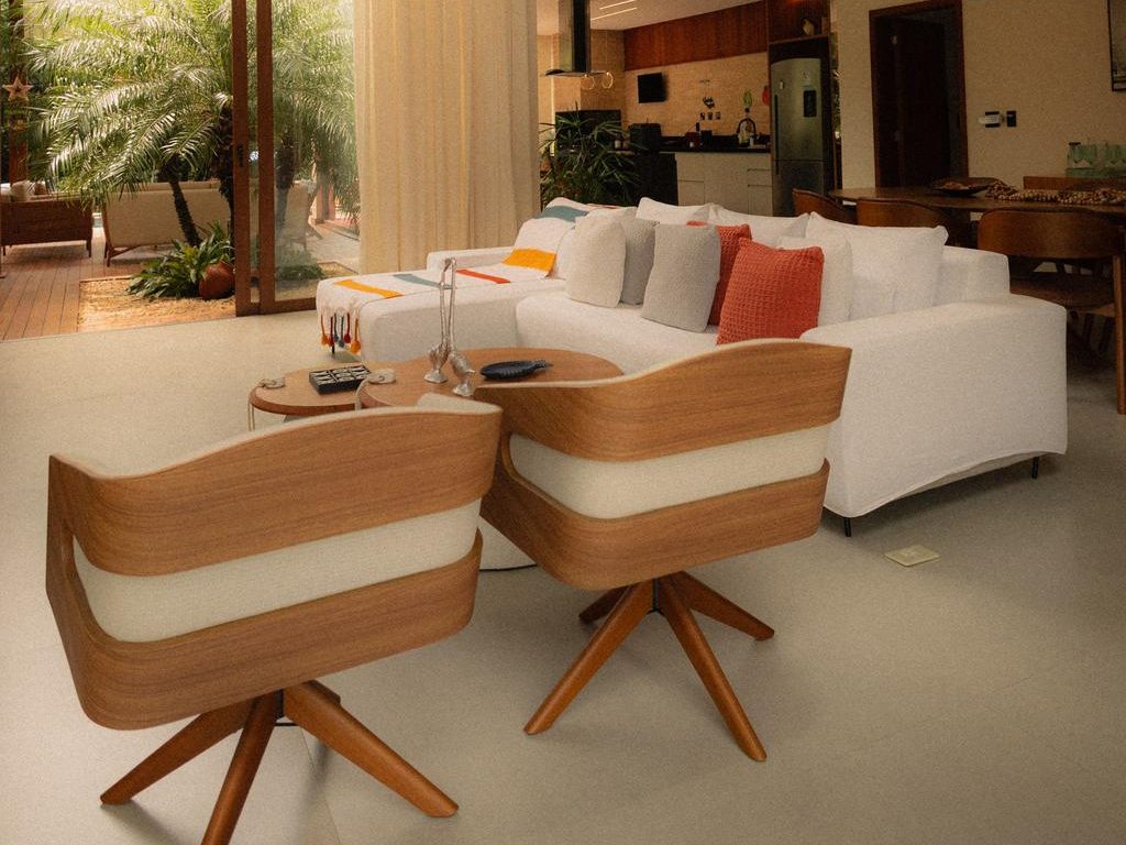 Two wood-framed swivel chairs with white cushions facing a white sofa in a bright double-height open-plan living room.