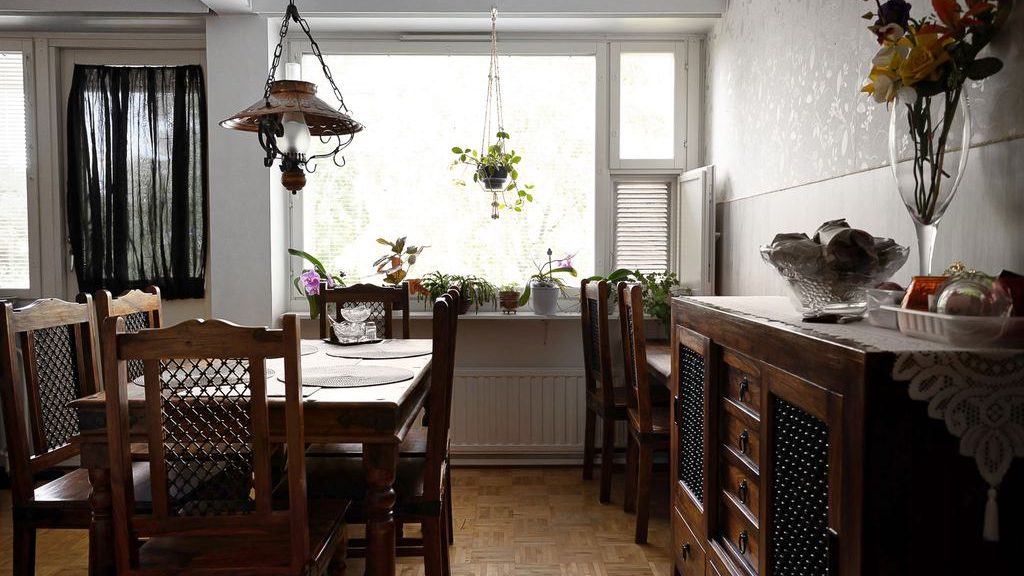 Traditional dining room with a dark wood buffet cabinet, lace runner, glass bowl, and plants near a window.