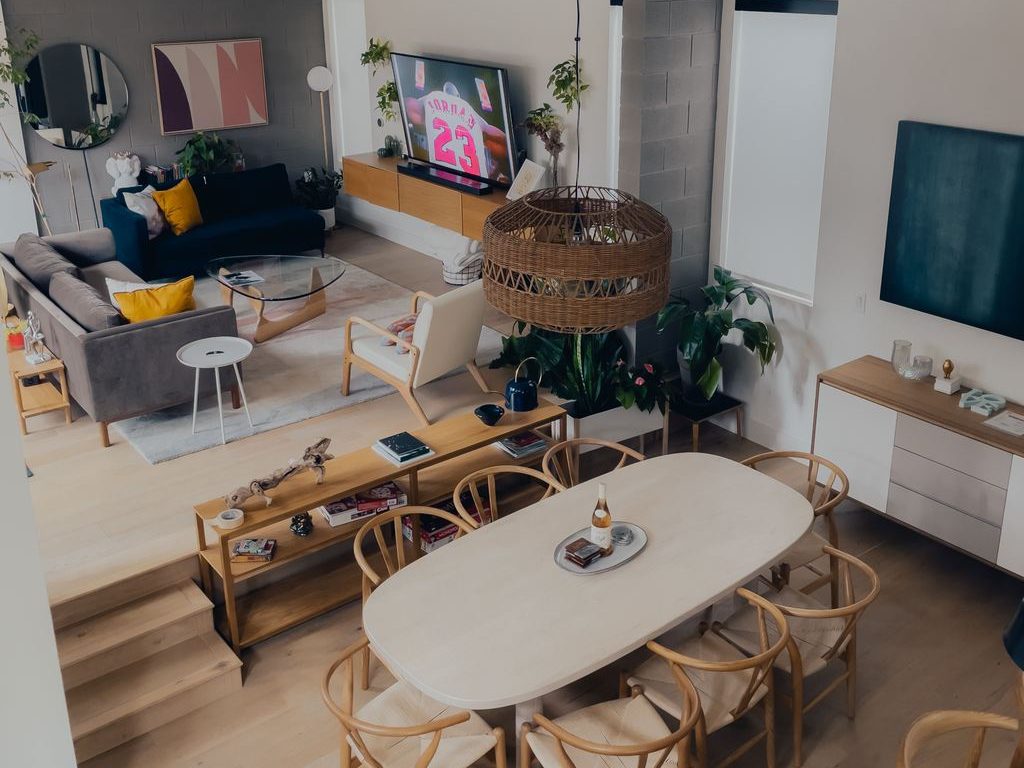 Scandinavian-inspired open-plan living and dining room with light wood floors, curved dining chairs, indoor plants, exposed beams, and cozy lounge seating.