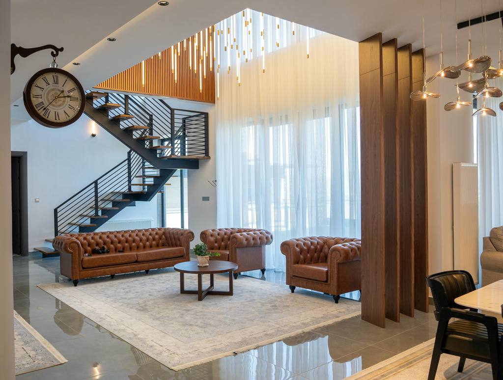 a luxurious loft with a black metal stair, three sofas, a round wood coffee table next to a dining room