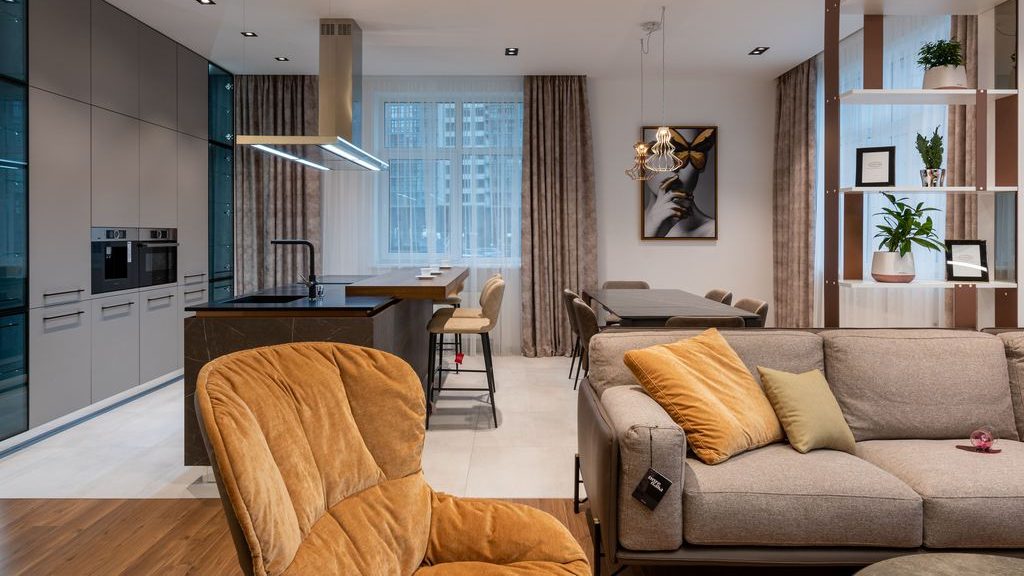 Tan swivel lounge chair beside a gray sofa in a modern open-plan living room with a kitchen and dining area.