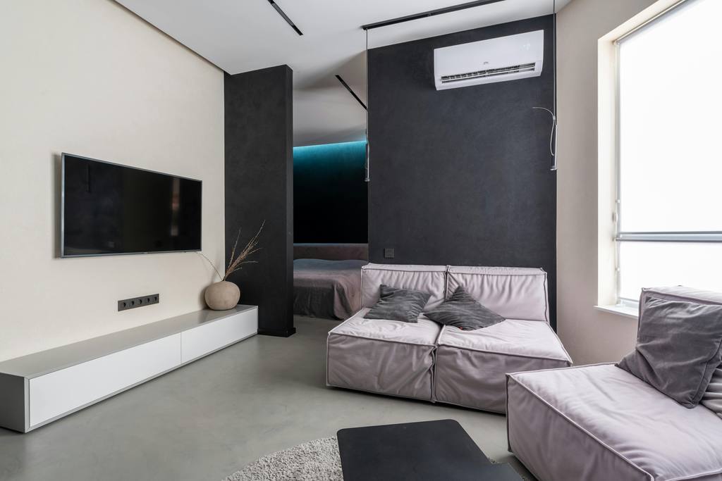 a minimalist black-and-white living room with a wall-mounted tv, a white media console, two grey sofas and a rectangular wood coffee table