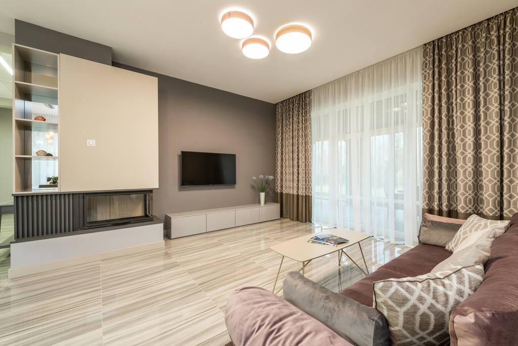 Modern living room with flush ceiling lights, low TV console, large curtains, and sectional sofa under soft ambient lighting.