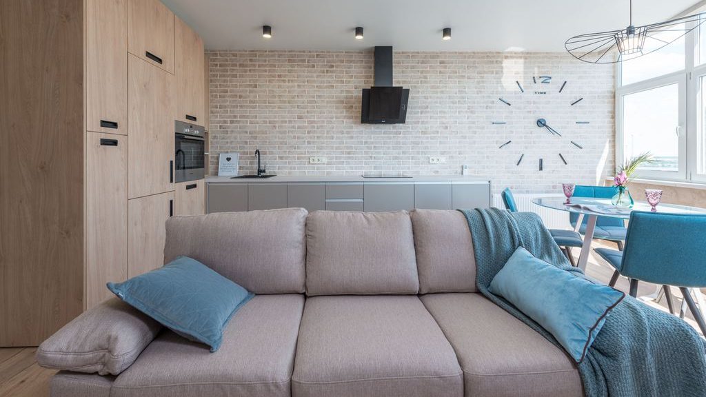 Light gray sofa with blue pillows and a throw blanket in an open-plan kitchen and dining area.