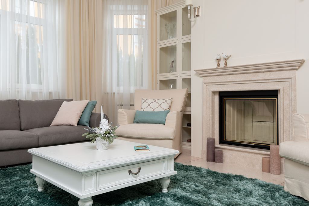 Elegant living room with gray sofa, cream armchairs, white coffee table, green shag rug, fireplace, sheer curtains, and soft neutral decor.