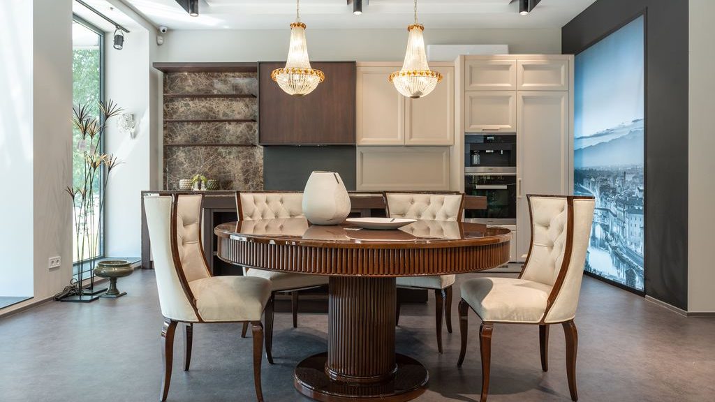 Round dark wood pedestal dining table with upholstered chairs, a low ceramic centerpiece, and two crystal pendant lights in a modern dining area.