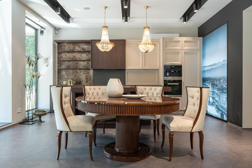 Transitional dining room with a round dark wood table, upholstered chairs, pendant chandeliers, and a modern open kitchen backdrop.