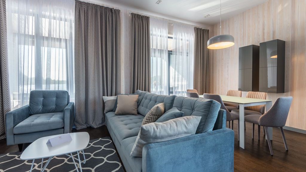 Renter-friendly open-plan living and dining room with blue sofa, patterned curtains, area rug, pendant light, and compact dining set.
