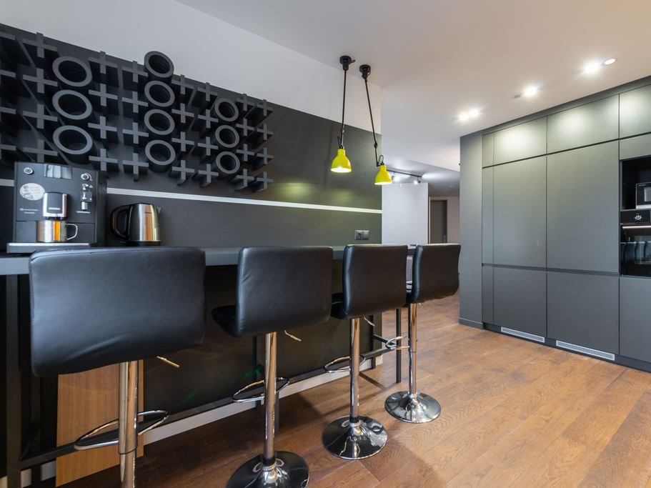 Modern kitchen coffee bar with black counter seating, built-in cabinets, coffee machine, kettle, pendant lights, and sleek dark finishes.