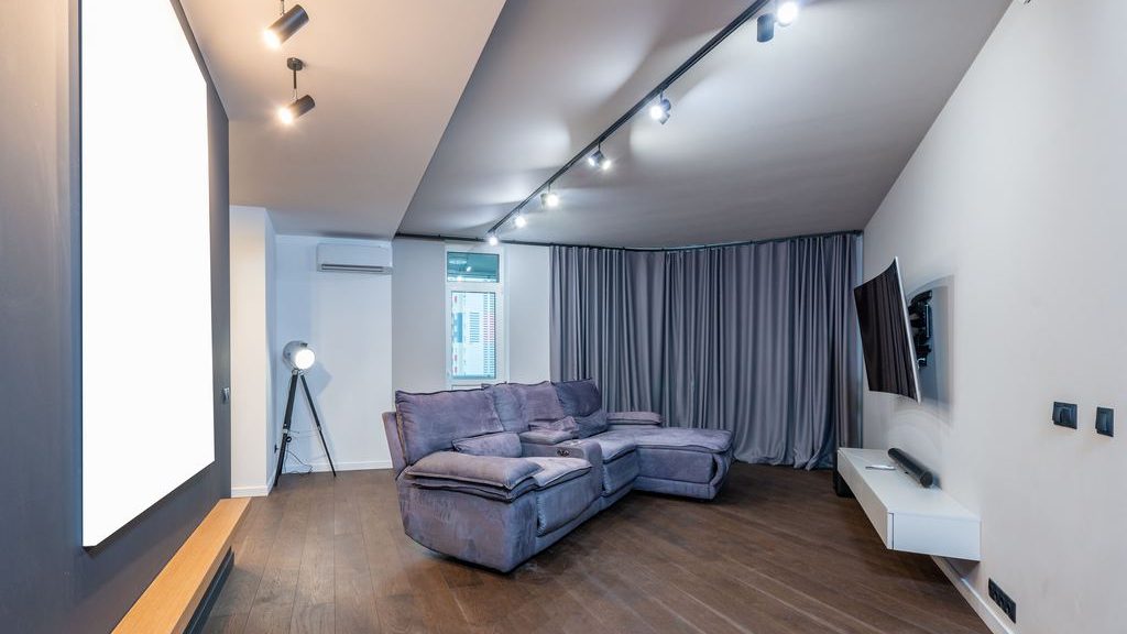 Modern media room with a gray reclining sectional facing a wall-mounted TV, floating console, and floor-to-ceiling curtains.