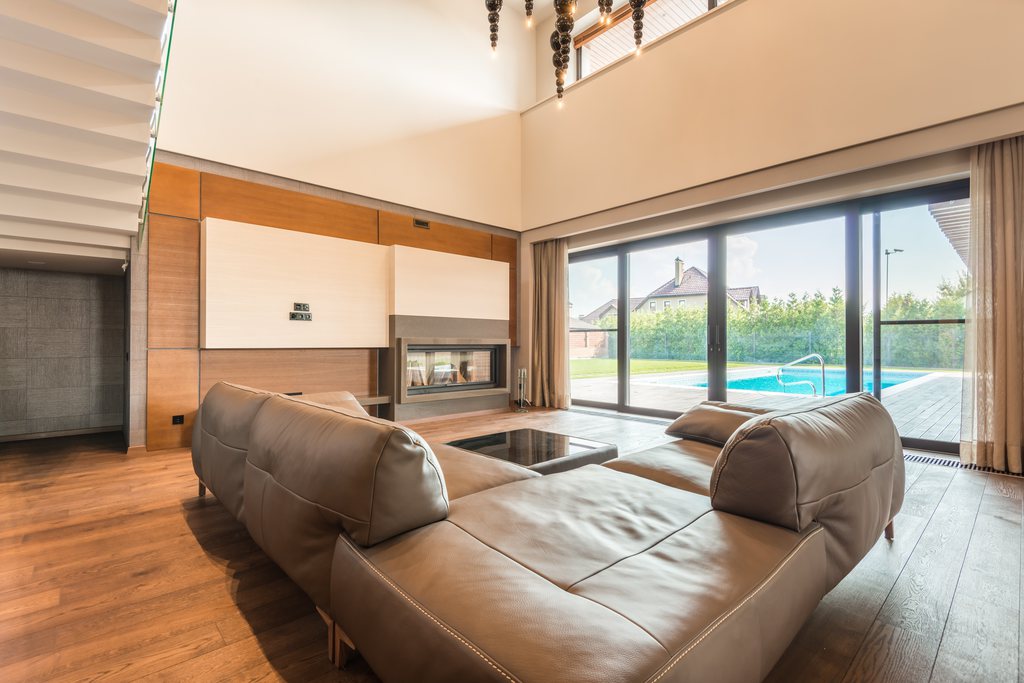 Modern leather sectional sofa in a bright living room with large glass doors, wood flooring, and a pool view outside.
