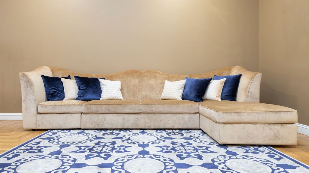 Beige sectional sofa with a chaise, navy and white pillows, and a blue patterned area rug in a neutral living room