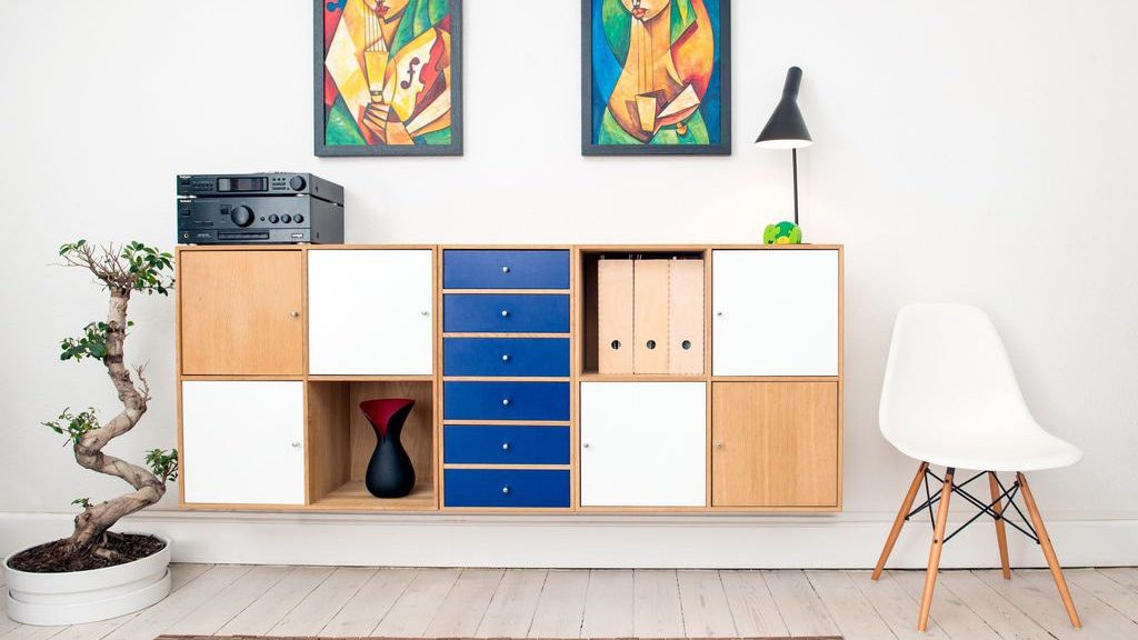 Colorful modular storage cabinet with drawers, doors, and open cubbies beneath framed artwork in a bright living room.