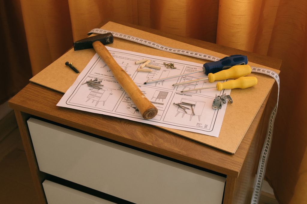 Tools, screws, assembly instructions, and a measuring tape arranged on a small wooden cabinet during furniture assembly.